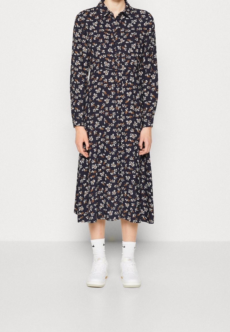 Abito lungo a maniche lunghe con stampa floreale navy, spacchettato con bottoni, colletto e falda svasata; abbinato a sneakers bianche e calzini alla caviglia coordinati.