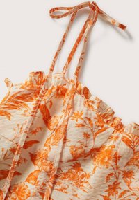 Top con stampa floreale caratterizzato da colori arancione e crema, tessuto leggero, spalline sottili, bordi volant e superficie strutturata.