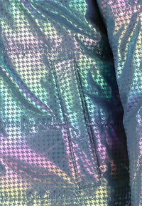 Iridescent jakke med et houndstooth-mønster, med en glat, reflekterende tekstur og en lomme på siden.