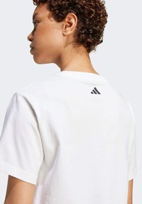 Vit bomullströja med rund ringning och korta ärmar. En liten svart Adidas-logotyp är placerad på baksidan nära ringningen.