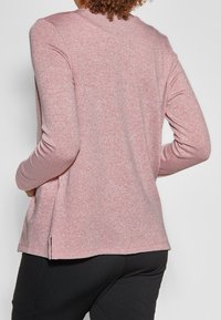 Long-sleeve pink sweater with a textured finish, featuring a rounded neckline and side slits at the hem. Elastic cuffs.