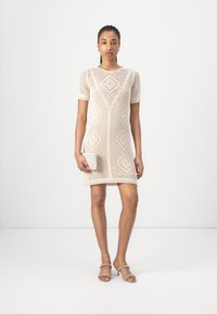 Knit short-sleeve dress in cream with diamond patterns and open weave. Paired with a textured clutch and minimal strappy heels.