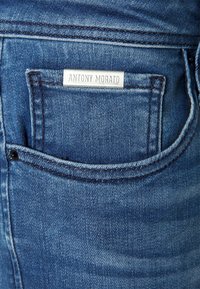 Modré džínové kalhoty se zadní kapsou s kovovým štítkem s nápisem "ANTONY MORATO". Textura je mírně opotřebovaná s kontrastním stehem.