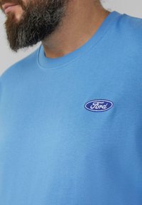Lichtblauwe katoenen sweatshirt met een ronde hals en een klein geborduurd ovaal logo in blauw en wit met de tekst "Ford" op de borst.
