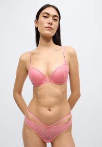 Ροζ δαντελένιο σουτιέν και ασορτί εσώρουχα με σχεδιασμό σε κυματιστές άκρες και γεωμετρικά μοτίβα, με ρυθμιζόμενους ιμάντες και ελάχιστες μεταλλικές λεπτομέρειες.