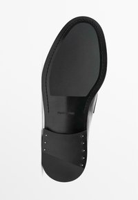 Sole di scarpa nera caratterizzata da una superficie liscia, forma curvilinea e dettagli in metallo lungo il lato. Presenza di branding inciso.