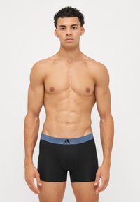 Črne bokserice z modrim elastičnim pasom, ki vsebujejo logotip Adidas. Gladka tekstura in prilegajoč dizajn.