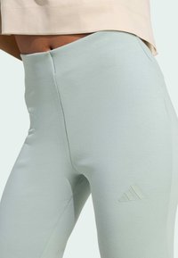 Jasno miętowe legginsy o gładkiej teksturze, z wysokim stanem i delikatnym wytłoczonym akcentem z logo po lewej stronie.