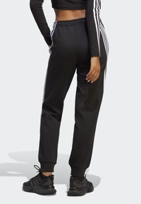 Čierne jogger nohavice so zúženým strihom, elastickým pásom a bielymi bočnými pruhmi. Skombinované s čiernymi športovými topánkami s textúrovaným dizajnom.