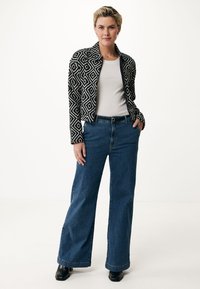 Svart- och vitmönstrad jacka med en figursydd design, ihop med blå vida denimjeans och svarta ankelkängor. Texturerade tyger, avslappnad stil.