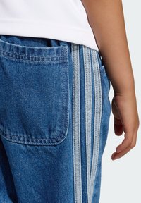 Joggers in denim con una tasca posteriore, tre strisce bianche sul lato e una vestibilità rilassata, realizzati in un tessuto liscio e leggermente strutturato.