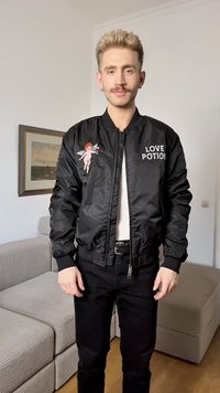Μαύρο bomber jacket με σατινέ φινίρισμα, με γραφικό του Έρωτα και κείμενο "LOVE POTION" μπροστά. Φορέθηκε πάνω από ένα λευκό πουκάμισο και μαύρο παντελόνι.