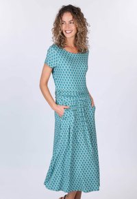 Ein türkisfarbendes, gemustertes Kleid mit kurzen Ärmeln, rundem Ausschnitt und Seitentaschen. Der Stoff fällt locker zu einem mittellangen Rock.