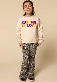Beige sweatshirt met "AUTUMN OF LOVE" in multicoulore letters, gecombineerd met liggende broek in panterprint. Zwarte sneakers maken de look compleet.