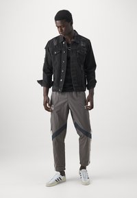 Chaqueta de mezclilla negra con detalles desgastados, combinada con pantalones deportivos grises que tienen rayas marinas y un logo, completado con zapatillas blancas.