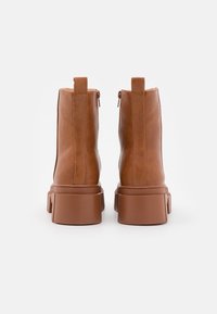 Stivali ankle in pelle marrone con suola spessa, texture liscia e chiusura con zip sul retro. Il tacco a blocco aggiunge altezza.