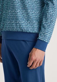 Sweatshirt à manches longues avec un motif géométrique en bleu et aqua, orné d'une bande unie bleu marine à l'ourlet. Associé à un pantalon bleu marine assorti.