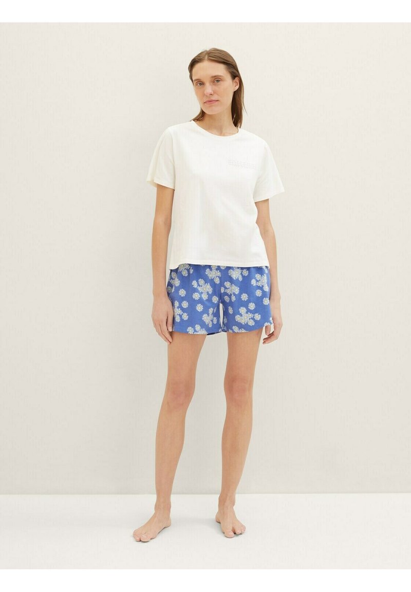 Camiseta blanca de manga corta con cuello redondo combinada con pantalones cortos de estampado floral azul. Tejido de algodón, ajuste casual, sin herrajes visibles.