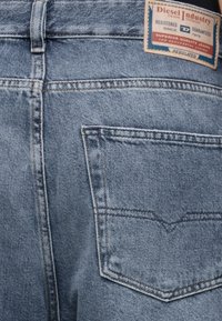 Μπλε τζιν denim κοντινή λήψη που δείχνει την πίσω τσέπη και μια ορθογώνια ετικέτα της μάρκας Diesel Industry ραμμένη στη μέση.