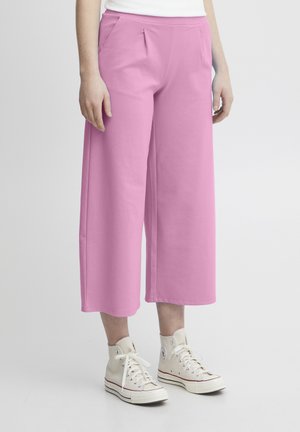 Pantalons larges rose clair en tissu doux, dotés de poches latérales et d'une coupe décontractée, associés à des baskets montantes blanches.