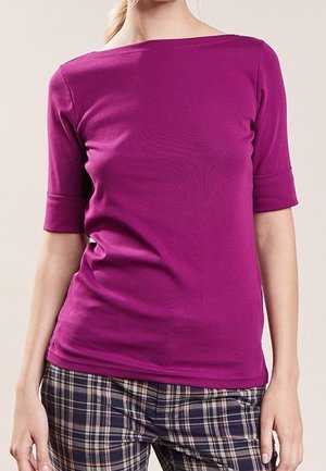 Woman wearing a fitted magenta boat-neck top with elbow-length sleeves and plaid pants in shades of navy, beige, and burgundy.
