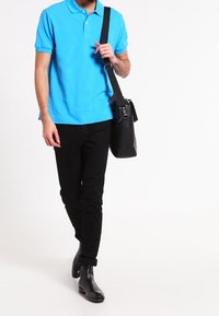 Ljusblå polo t-shirt, svarta slim-fit byxor och svarta läderkängor. En svart axelväska bärs över kroppen.