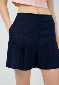 Pantalones cortos azul marino hechos de tejido texturizado, con bolsillos laterales y diseño plisado, cortados por encima de la rodilla, con un ajuste relajado.