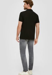Zwarte polo shirt, korte mouwen, klassieke kraag, van katoen. Gepaard met grijze jeans en witte sneakers, weergegeven van achter.