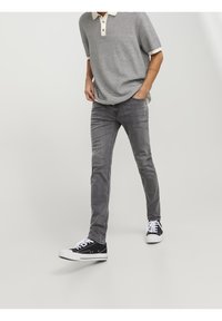 Vaqueros gris slim-fit con un ligero desvanecimiento, combinados con una camiseta polo a rayas en blanco y negro con cuello beige y tres botones. Zapatillas negras.