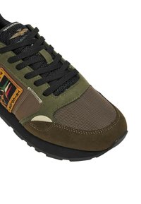 Sneaker front in verde oliva e marrone con lacci neri, punta in rete, dettagli in suede e un patch ricamato colorato sul lato.