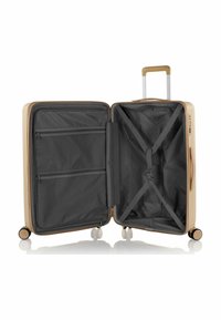 Valigia rigida in oro, con un interno aperto caratterizzato da rivestimento nero, tasche a rete con zip e cinghie di compressione. Quattro ruote e maniglia telescopica.