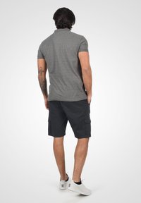 Polo shirt gri cu mânecă scurtă, asortat cu pantaloni scurți cargo închiși la culoare. Modelul poartă adidași albi. Caracteristicile includ un guler clasic și pantaloni scurți cu buzunare.