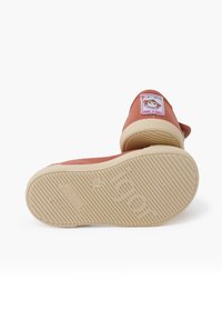 Scarpa da ginnastica rosa in tela con punta rotonda, fascia elastica e suola in gomma beige. Presenta un'etichetta colorata sul tacco con un design a cartone animato.