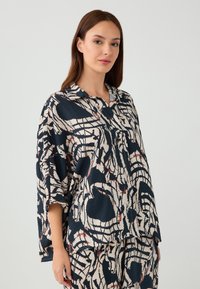 Blusa ampia blu navy con un motivo astratto crema e ruggine, caratterizzata da un collo alla francese e maniche a 3/4, realizzata in un tessuto morbido.