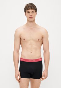 Mustat puuvillaiset bokserishortsit, joissa on punainen vyötärönauha jossa lukee "Calvin Klein" -logo. Malli on istuva ja sileäpintainen.