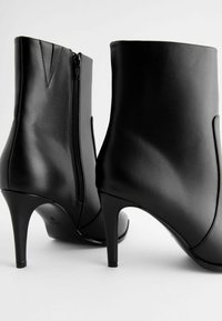 Bottines en cuir noir avec un talon haut, dotées d'une fermeture éclair sur le côté et d'accents de coutures verticales pour plus de détails et de design.