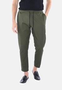 Pantaloni jogger tapered verde oliva con cintura elastica, chiusura con lacci, tasche laterali e una texture di tessuto leggero.