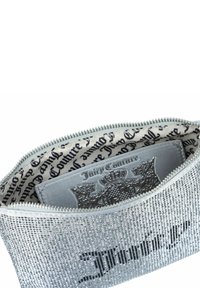 Sidabrinis blizgučių rankinukas su užtrauktuku, kuriame matomas juodas logotipas ir raštuota audinio vidinė dalis, demonstruojanti „Juicy Couture“ prekės ženklą.