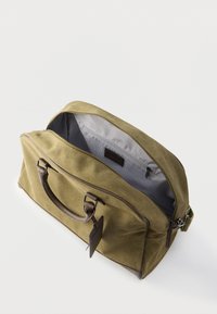 Sac de sport en toile vert olive avec des accents en cuir brun ; comprend un dessus zippé, deux poignées solides et une doublure intérieure rayée.