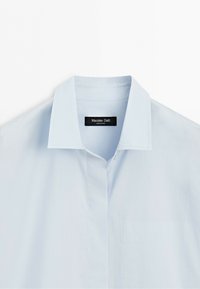Světle modrá košile na knoflíky s špičatým límcem a štítkem značky Massimo Dutti uvnitř výstřihu.