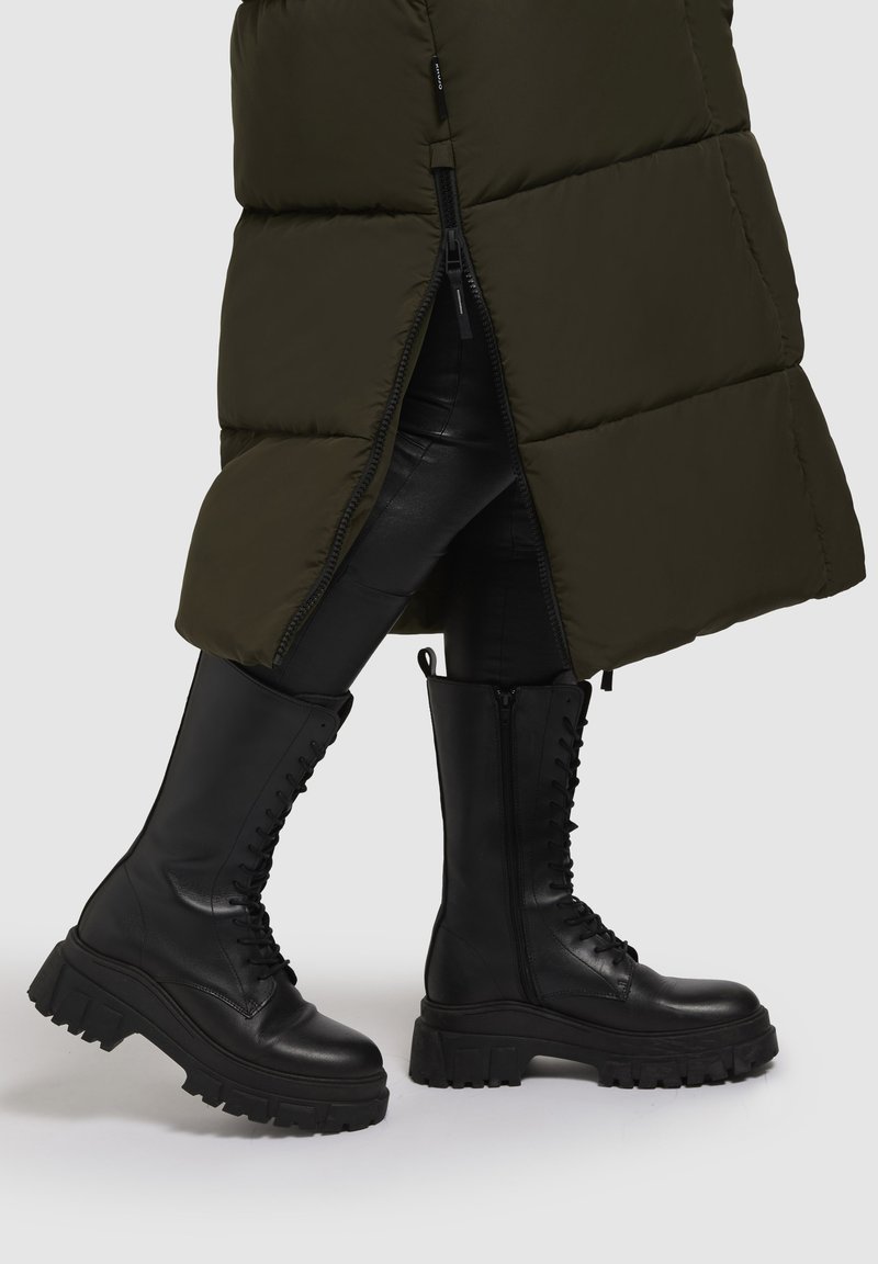 Schwarze Kampfstiefel haben eine dicke Sohle, eine Schnürung vorne und einen Reißverschluss an der Seite. Sie bestehen aus glattem Leder mit mattem Finish und robuster Textur.
