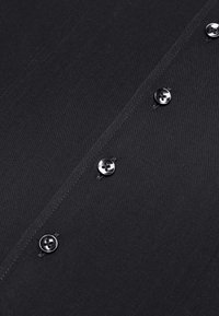 Schwarzes Hemd aus strukturiertem Stoff, mit sechs glänzenden Knöpfen entlang der Knopfleiste und subtilen Nahtdetails.