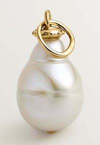 Colgante de perla con superficie brillante, forma de lágrima y un acento dorado en la parte superior que presenta un lazo decorativo para su sujeción.