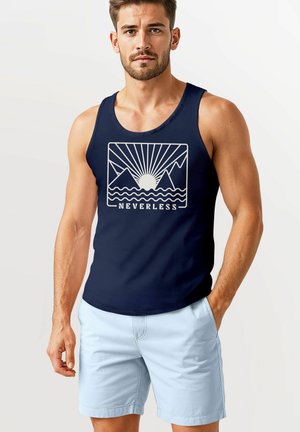 Marine Tanktop mit grafischem Muster von einem weißen Berg und der Sonne. Merkmale einen runden Halsausschnitt und ärmelloses Design. Kombiniert mit hellblauen Shorts.