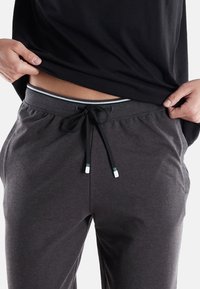 Dark gray sweatpants with an elastic waistband, adjustable drawstring with green and white accents, and soft texture, paired with a black top.