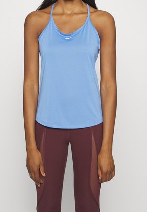 Mujer que lleva una camiseta sin mangas Nike azul claro y leggings burdeos con paneles de malla, de pie sobre un fondo blanco liso.