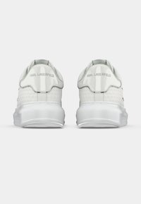 Hvite joggesko med en teksturert mesh-overdel, glansfulle patent-detaljer og en dempet såle. Har merkevarelogo på hælen.