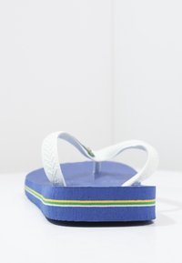 Modré žabky s strukturovaným bílým popruhem, který má zelený a žlutý pruh kolem podrážky. Materiál vypadá gumově a lehce.