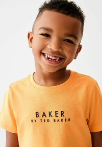 Orange bomulds T-shirt med rund halsudskæring, der har et sort trykt logo "BAKER BY TED BAKER" på fronten. Korte ærmer og glat tekstur.