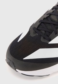 Black athletic shoe with a textured upper, featuring white accents, flat laces, and a reinforced toe cap. Lightweight design with a cushioned sole.